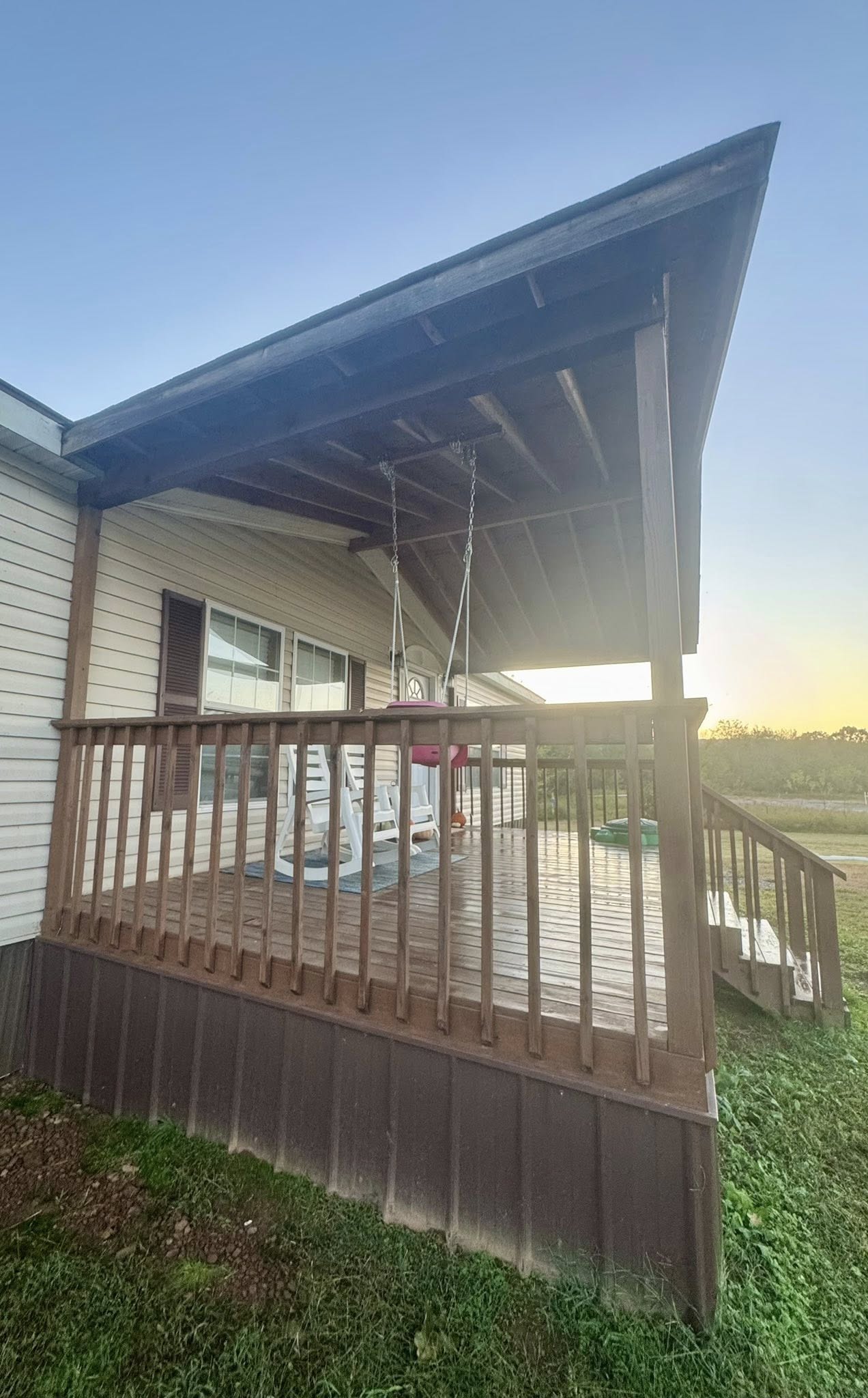 A cozy porch with a wooden railing and sloped roof. Two white rocking chairs and a porch swing create a relaxed atmosphere against a serene sunset sky.
