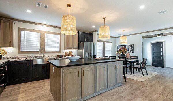 Spacious kitchen with a large wooden island, wicker pendant lights, stainless steel appliances, and a dining table in a bright, airy setting.