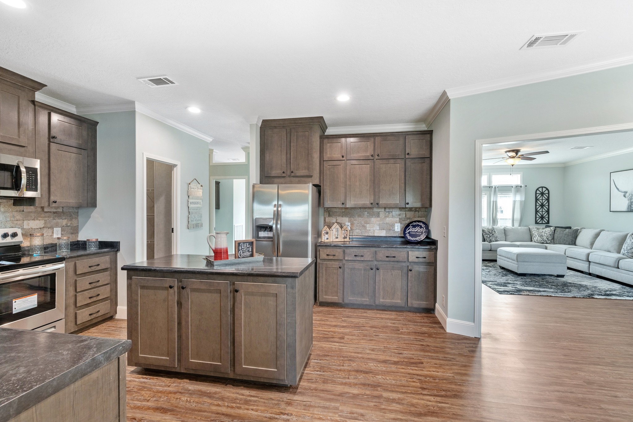 Spacious kitchen featuring wooden cabinets, island with dark countertop, stainless steel fridge, and adjacent cozy living room with a large sectional sofa.