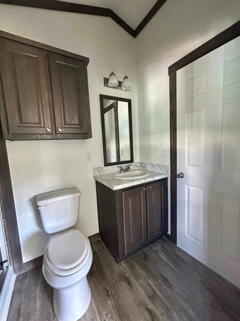 Compact bathroom with wood accents; features a toilet, dark wood cabinets, marble countertop, mirror, and soft lighting, creating a cozy atmosphere.