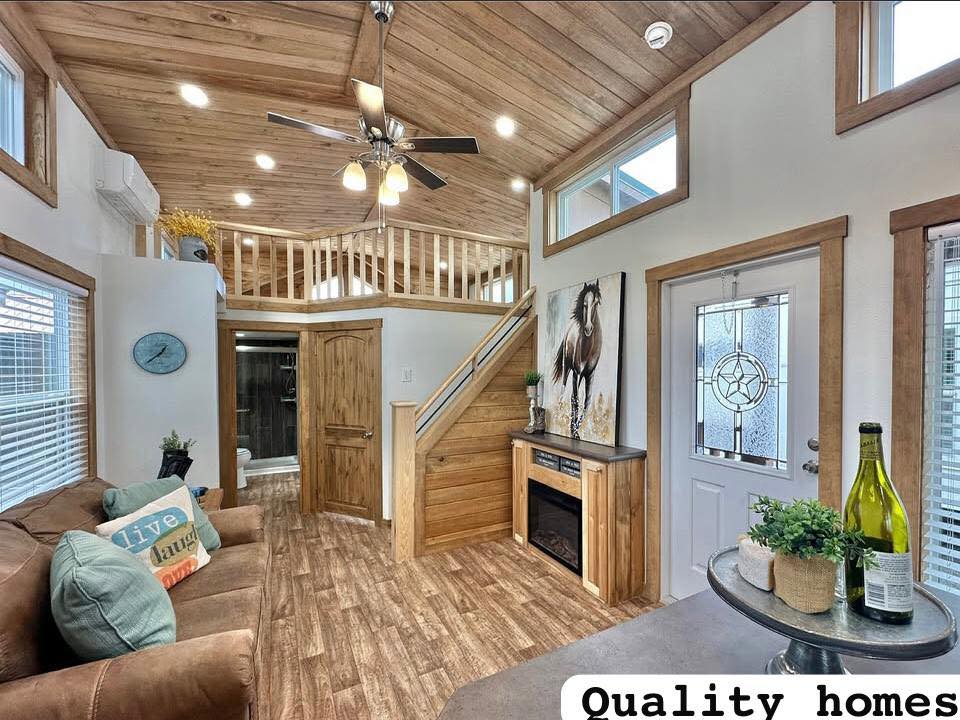 Cozy rustic living room with wood ceiling and floor, brown couch, decorative pillows, horse painting, fireplace, and loft. Bright and inviting.