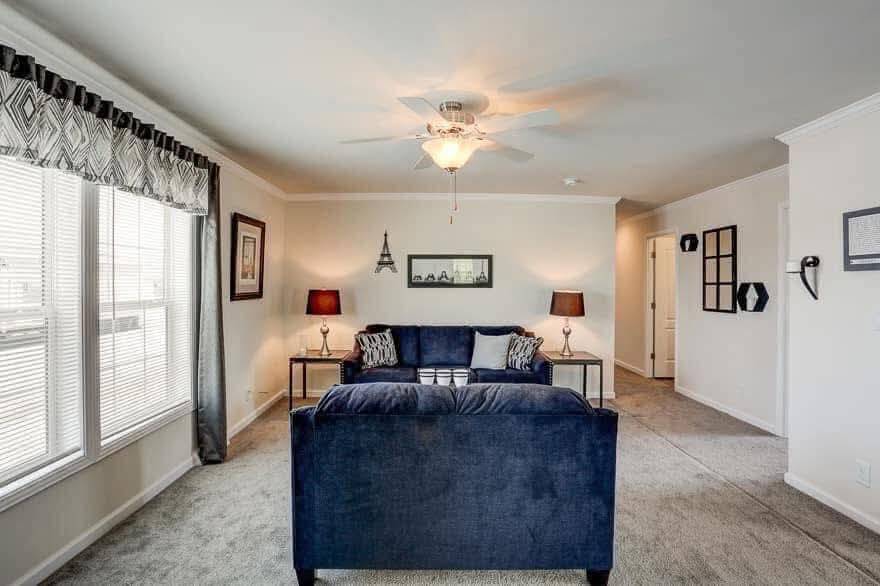 A cozy living room with a dark blue sofa and patterned cushions, flanked by two side tables with red lamps. Artwork and decor add a touch of elegance, with soft natural light streaming through large windows.