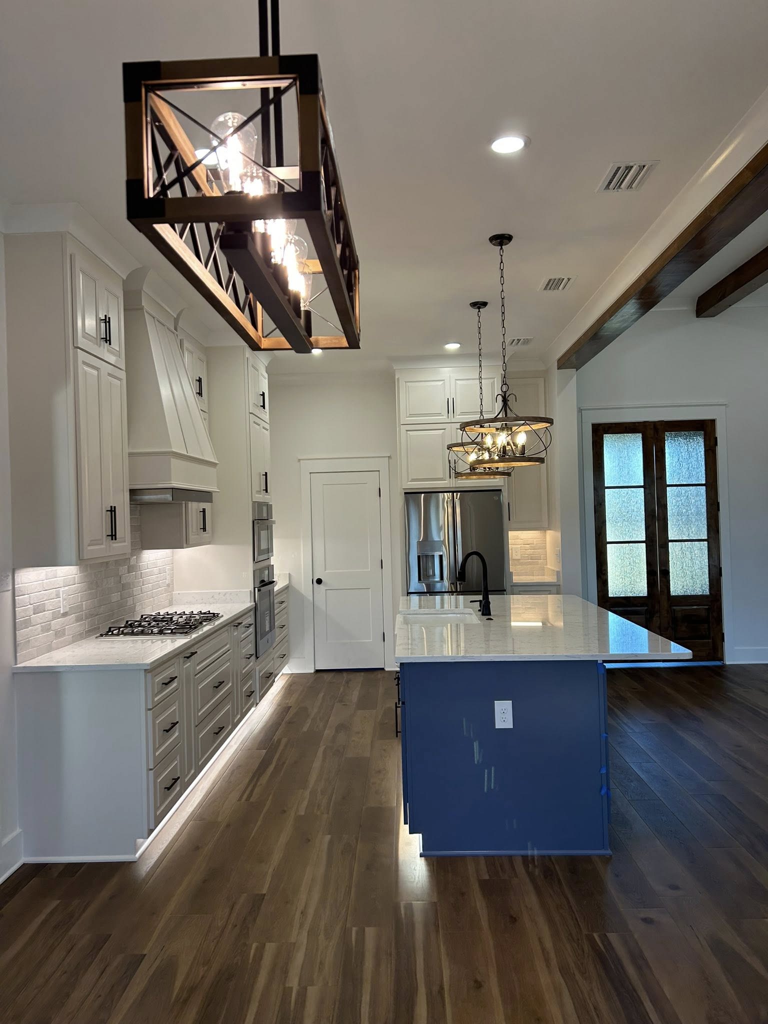 Modern kitchen with white cabinets, a blue island, and wood floors. Stylish pendant lights hang above. Stainless steel appliances add a sleek touch.