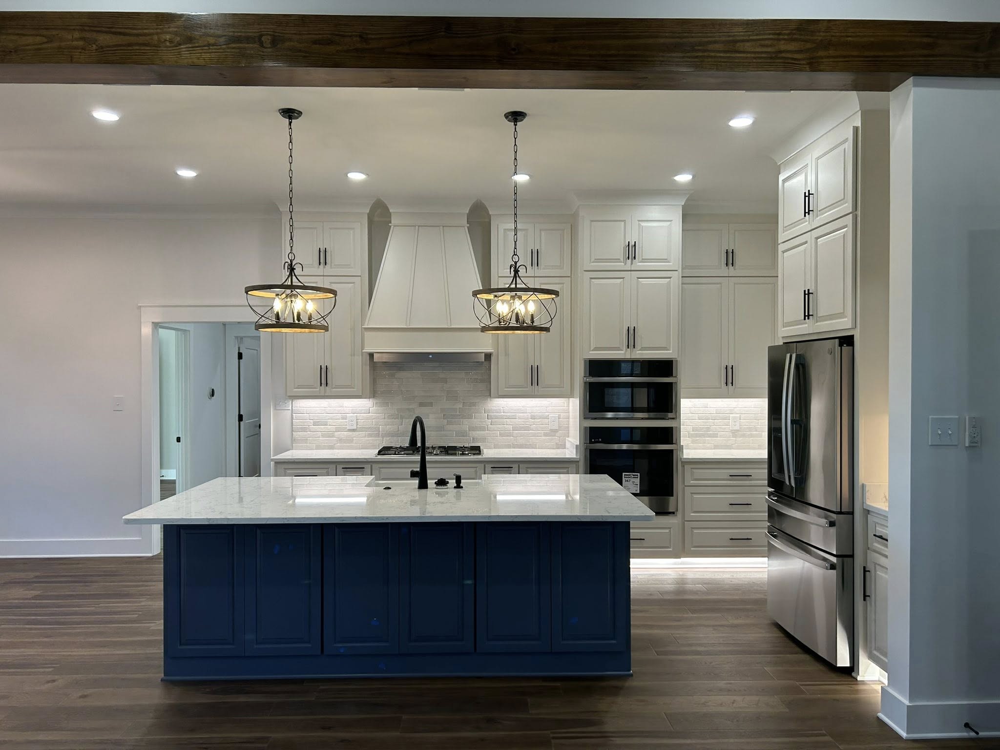 Modern kitchen with dark wood floors, white cabinets, and a blue island. Two ornate pendant lights hang above the marble countertop, exuding elegance.