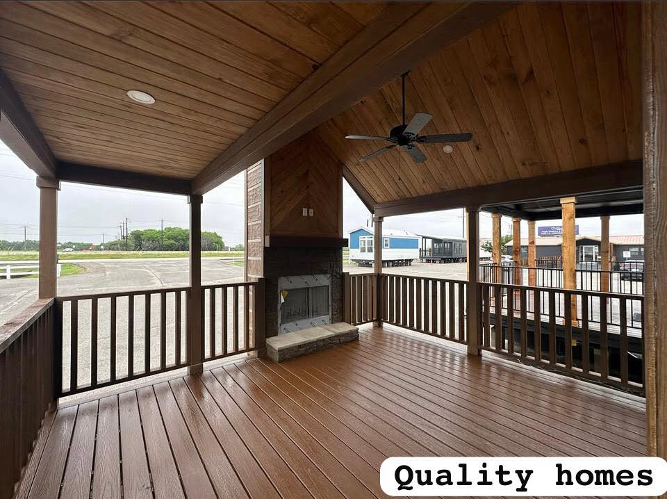 Covered wooden patio with vaulted ceiling, ceiling fan, and fireplace. It overlooks a parking lot and nearby homes. Text reads "Quality homes."