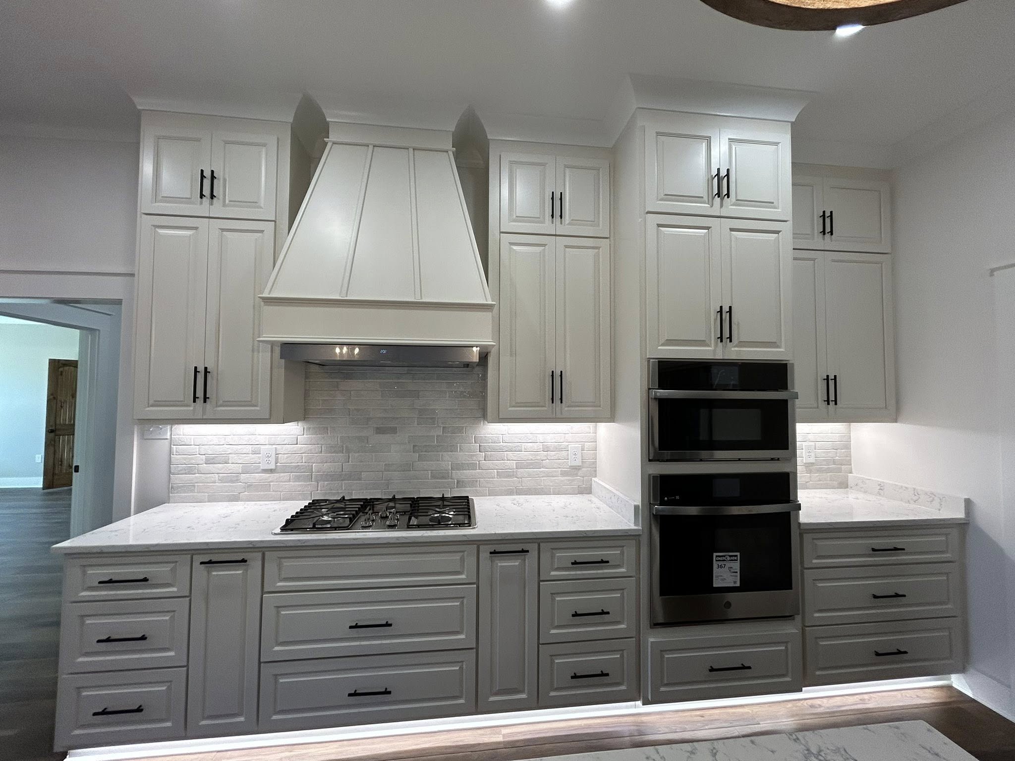 Modern kitchen with light gray cabinets, a stainless steel range hood, and a black oven. Bright backsplash and marble countertops accentuate the sleek design.