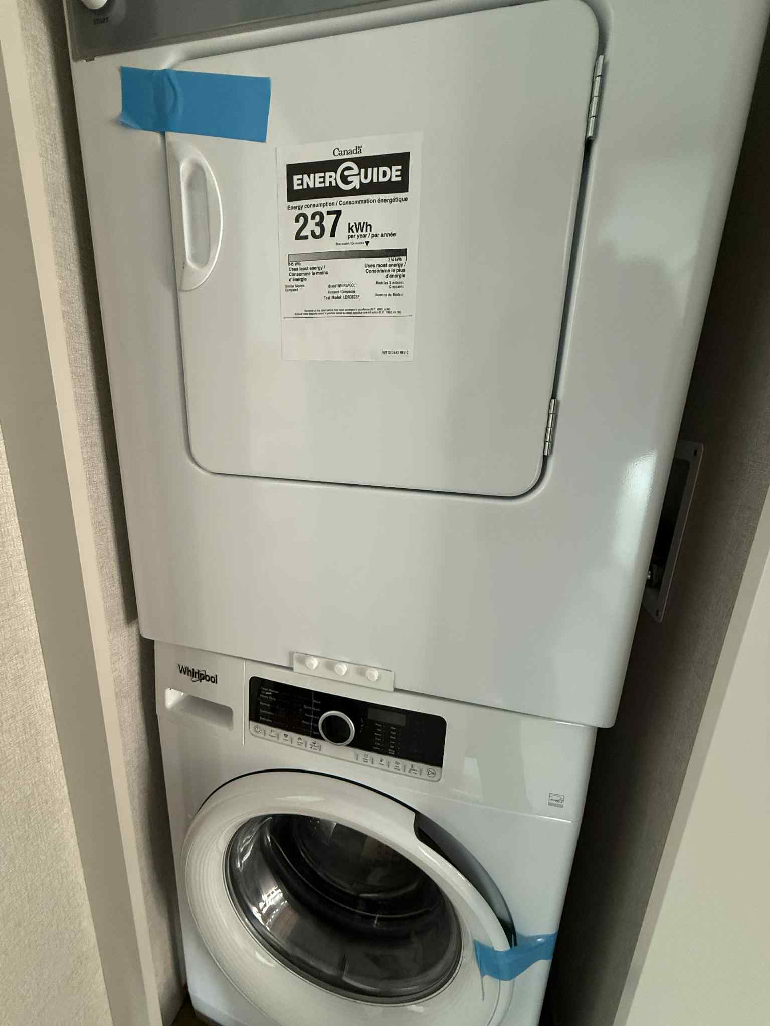 Stacked white washer and dryer in a compact space. A Canadian EnerGuide label, showing 237 kWh, is taped on the dryer door. Clean and efficient.