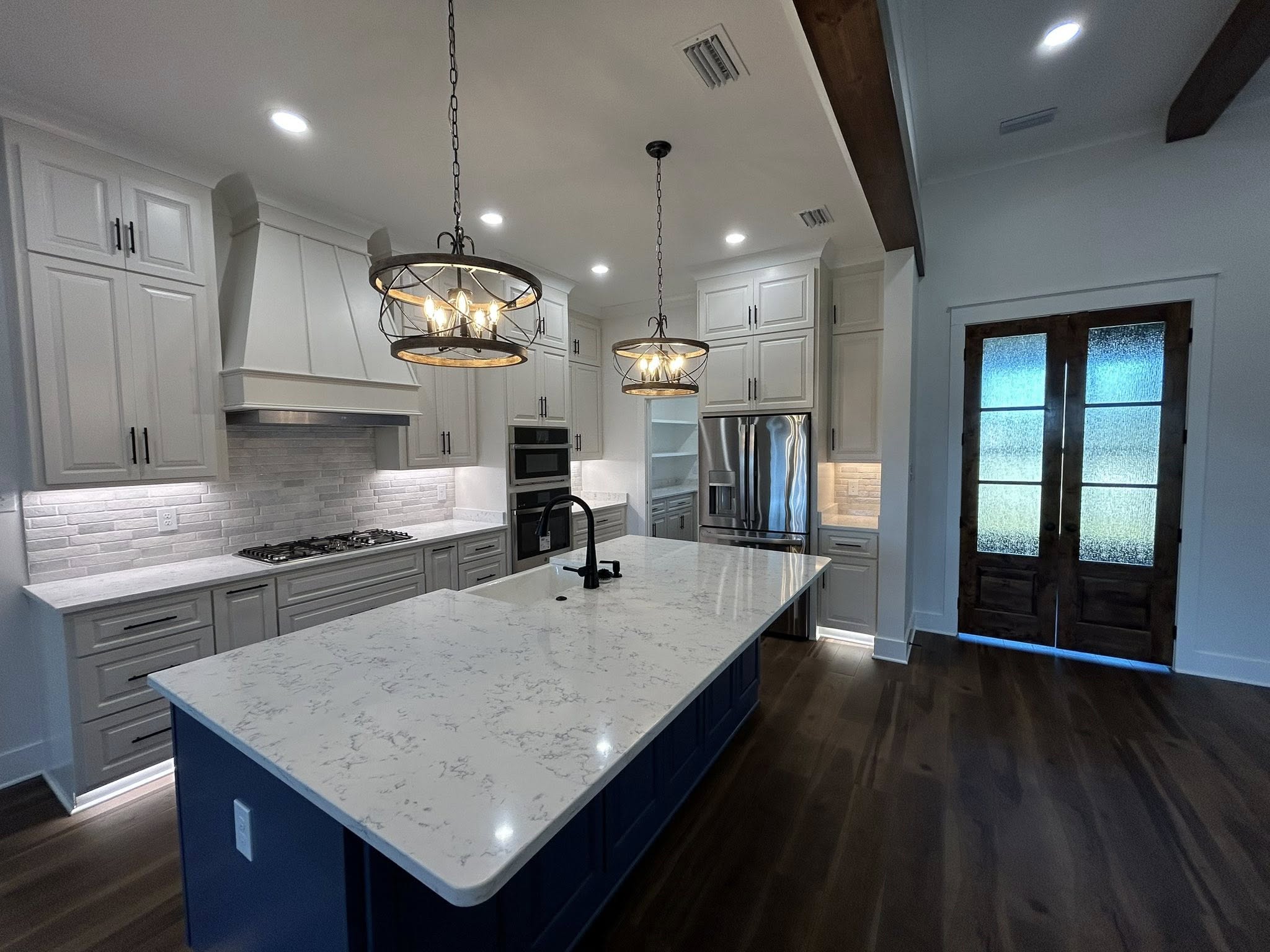 A modern kitchen with a large marble island and dark wood base, pendant lights, white cabinets, stainless steel appliances, and wooden floors. Cozy and elegant.
