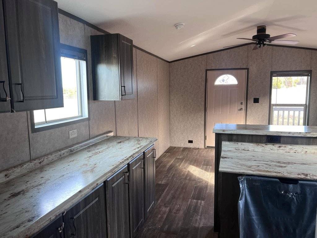 Modern kitchen interior with dark wood cabinets, marbled countertops, and laminate flooring. Sunlight filters through a window, creating a cozy ambiance.