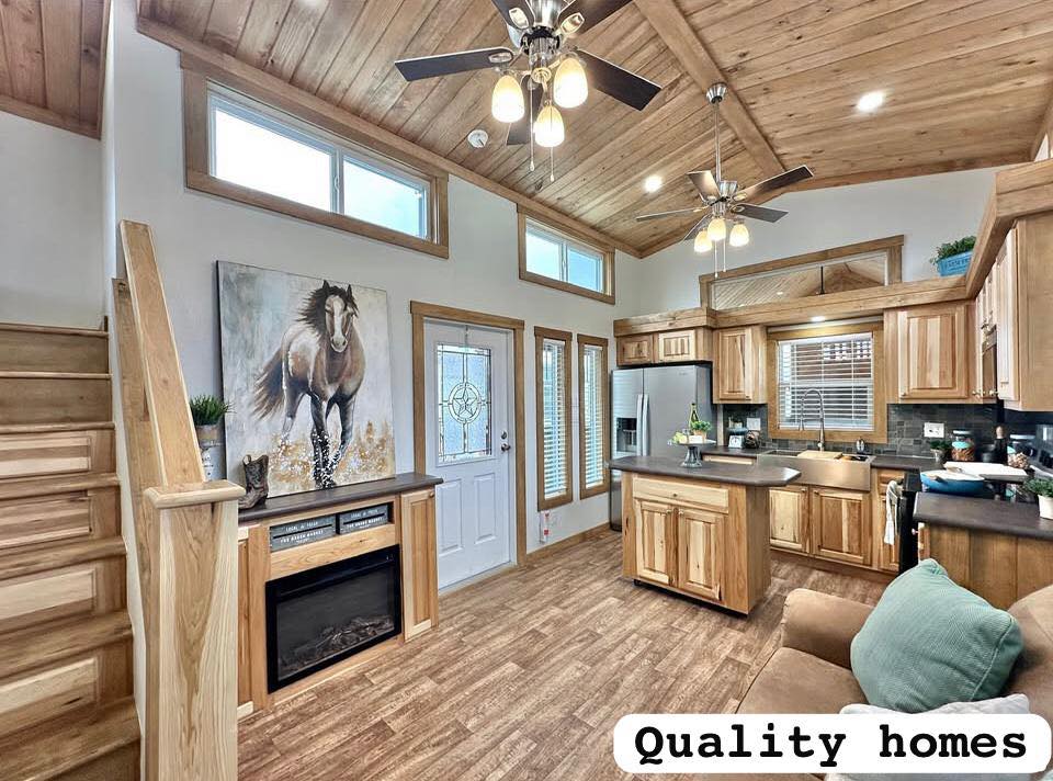 Warm, rustic interior featuring wooden ceilings and floors, cozy kitchen with wooden cabinets, island, large horse painting, and "Quality homes" text.