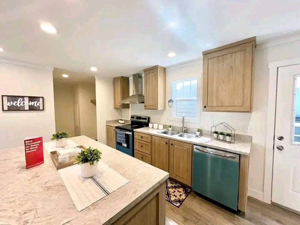 Bright, modern kitchen with light wood cabinets, stainless steel appliances, and a marble island. A welcoming sign adds warmth. Cozy and inviting ambiance.