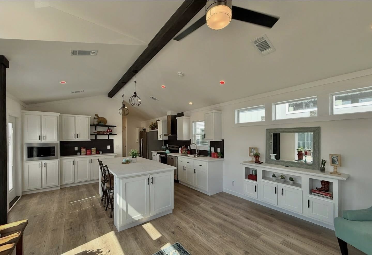 A modern kitchen with white cabinets, a central island, and wooden accents. Natural light fills the space, creating a warm and inviting atmosphere.