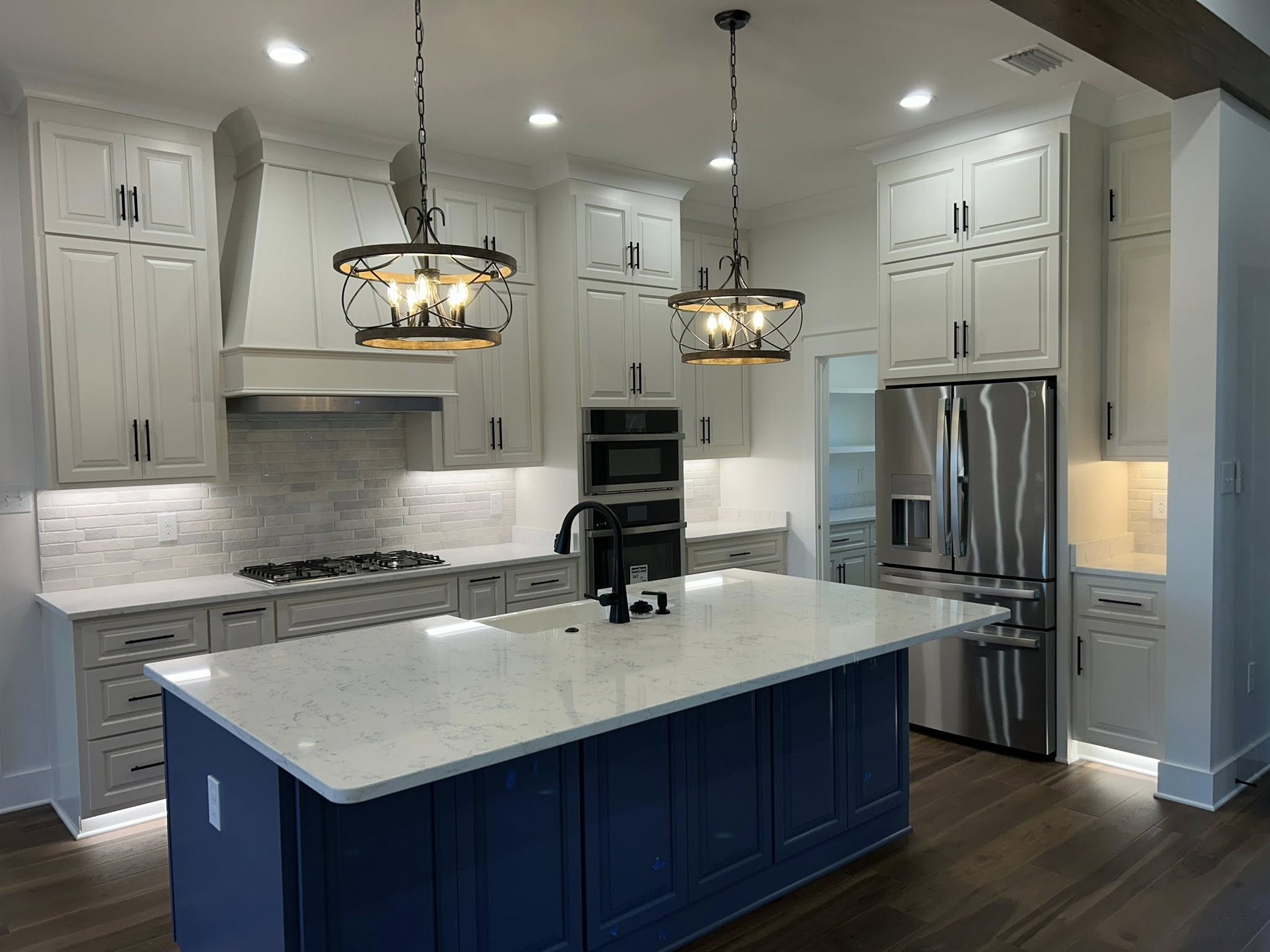 Modern kitchen with white cabinets, stainless steel appliances, and a large central island with a blue base. Two pendant lights add warmth.
