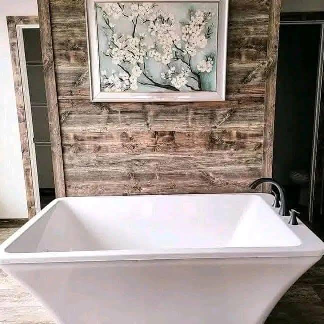 Freestanding white bathtub against a rustic wooden wall. Above, a painting of white blossoms adds elegance. The setting feels serene and inviting.