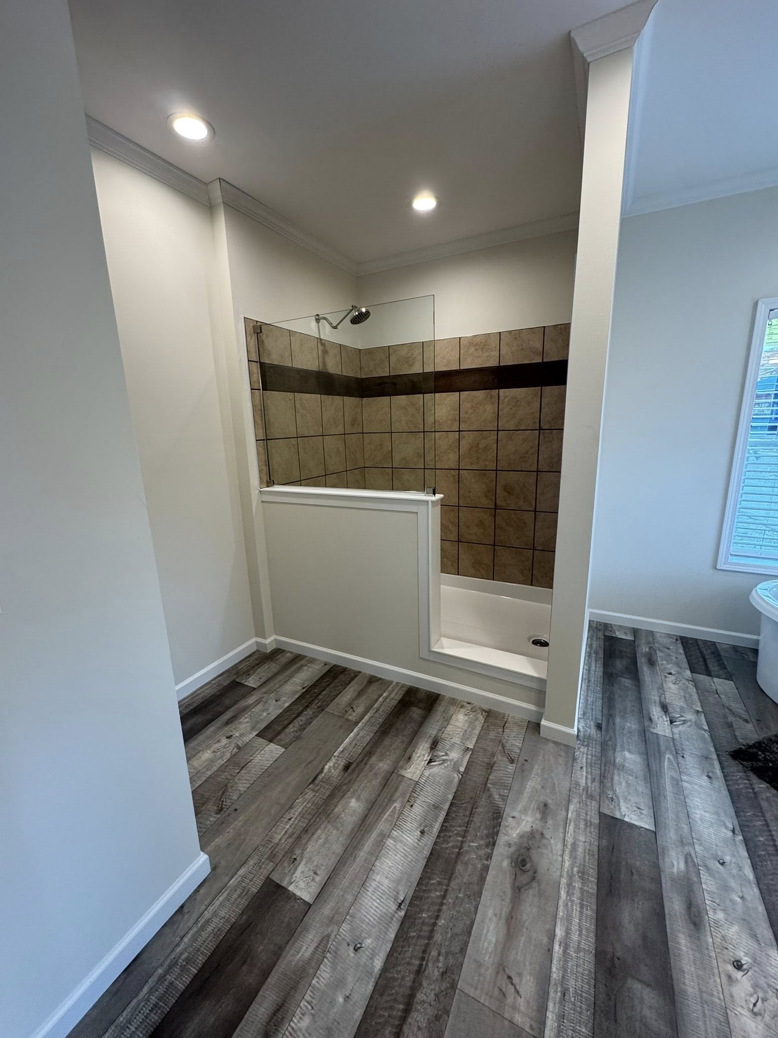 Modern bathroom with a step-in tiled shower featuring muted brown tiles and a glass panel. Gray wood-style flooring adds a sleek, contemporary touch.