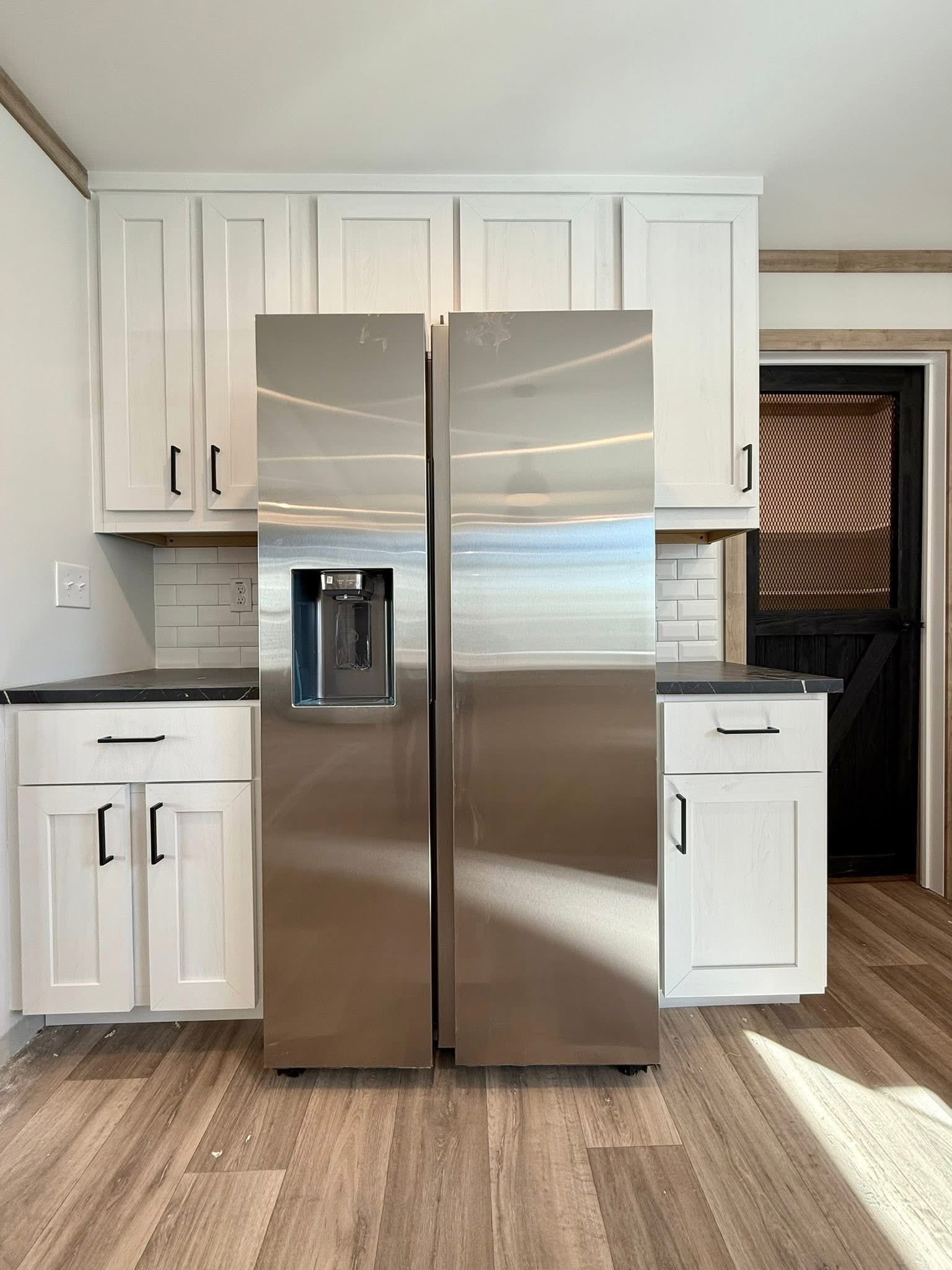 Modern kitchen featuring a sleek stainless steel refrigerator with a water dispenser, surrounded by white cabinets and a light wood floor, creating a clean and fresh ambiance.