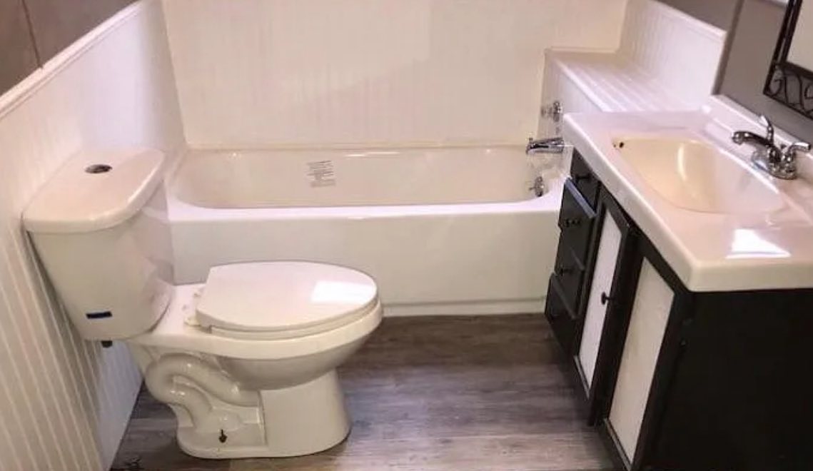Compact bathroom with a white toilet beside a bathtub. A sink with a mirror and dark vanity contrasts with light wood flooring, creating a neat, modern look.
