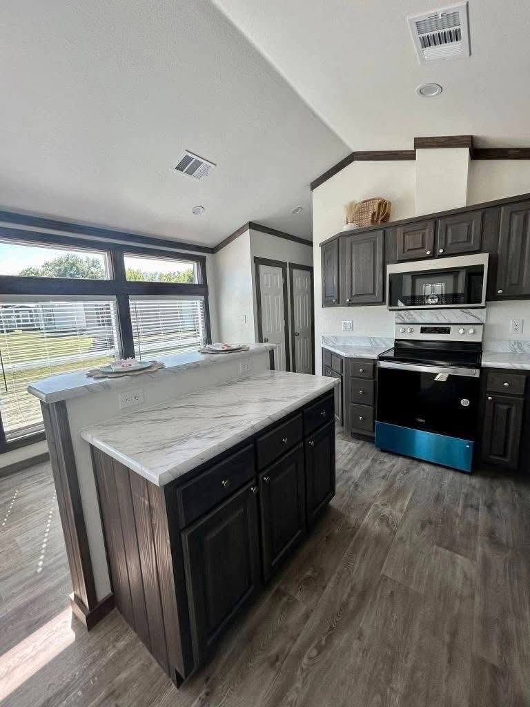 Modern kitchen with dark wood cabinets, white marble countertops, stainless steel appliances, and large windows offering natural light. Cozy and bright.