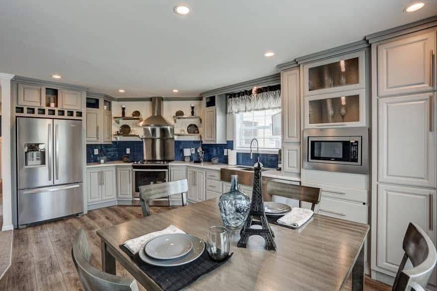 Spacious kitchen with cream cabinetry, stainless steel appliances, and blue tile backsplash. A dining table features plates, glasses, and an Eiffel Tower model.
