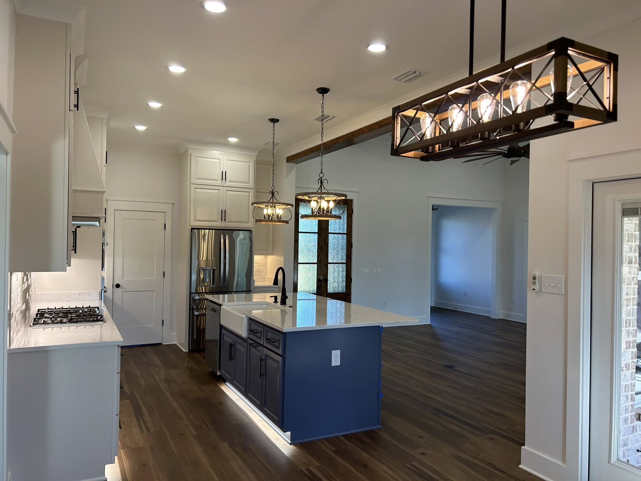 A modern kitchen with a white and blue island under elegant pendant lighting. Stainless steel appliances, wooden floors, and a cozy, inviting ambiance.