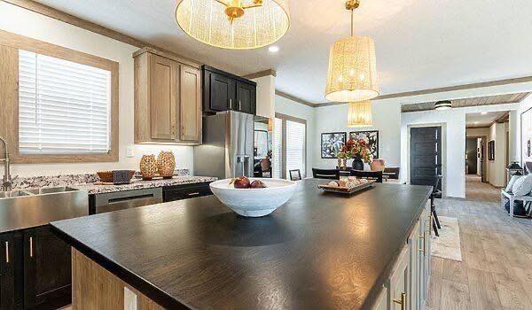 Modern kitchen with a large black island countertop, wooden cabinets, pendant lights, and stainless steel appliances. Warm, inviting atmosphere.