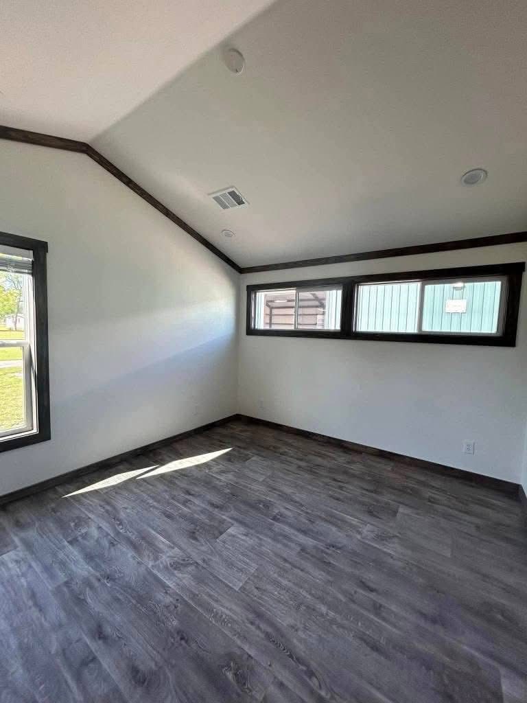 Simple, unfurnished room with white walls and dark wooden floor. Sloped ceiling and narrow windows add a modern touch. Natural light streams in gently.