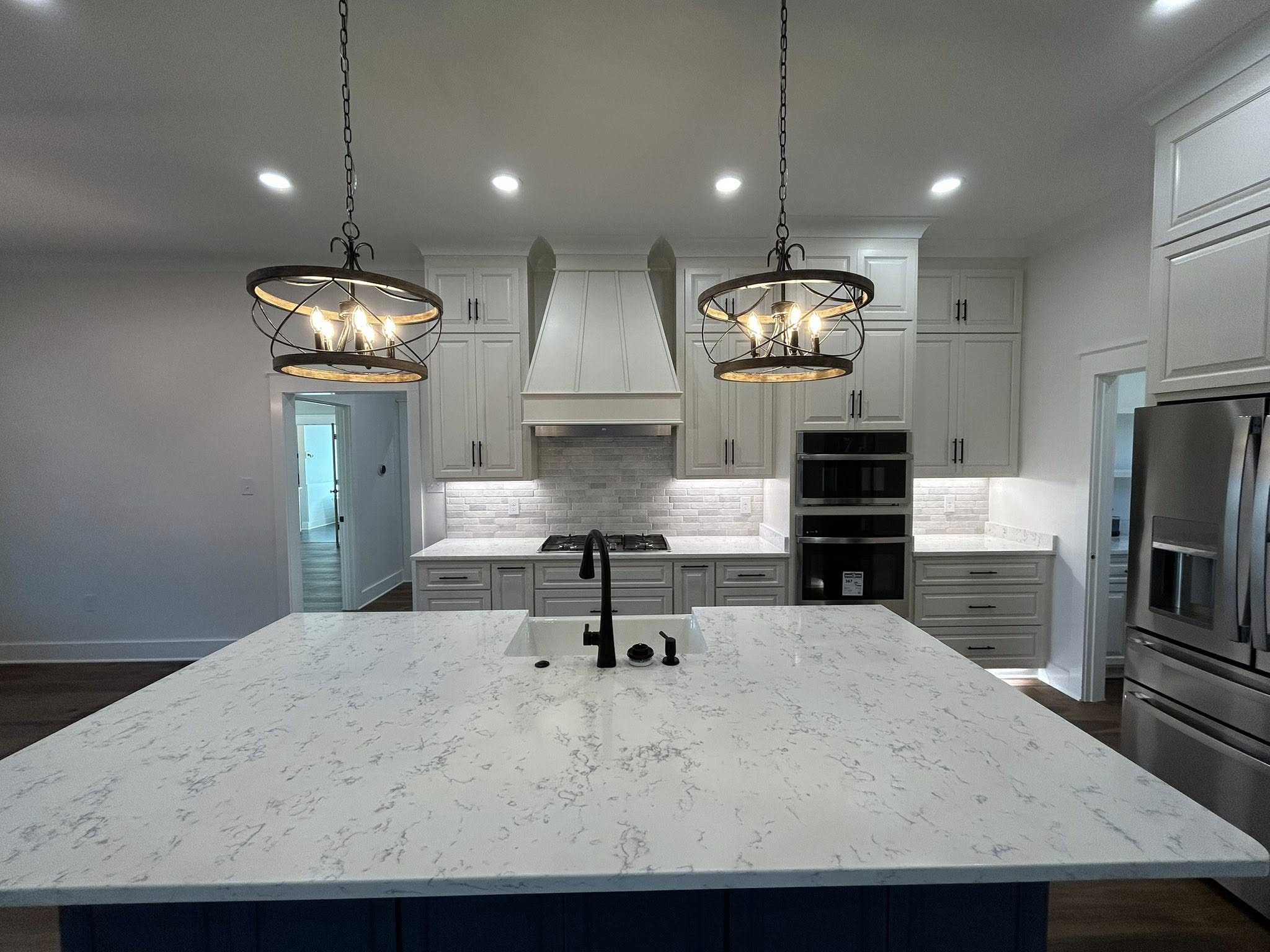 Modern kitchen with a large marble island featuring a black faucet, two industrial-style pendant lights, stainless steel appliances, and white cabinetry.