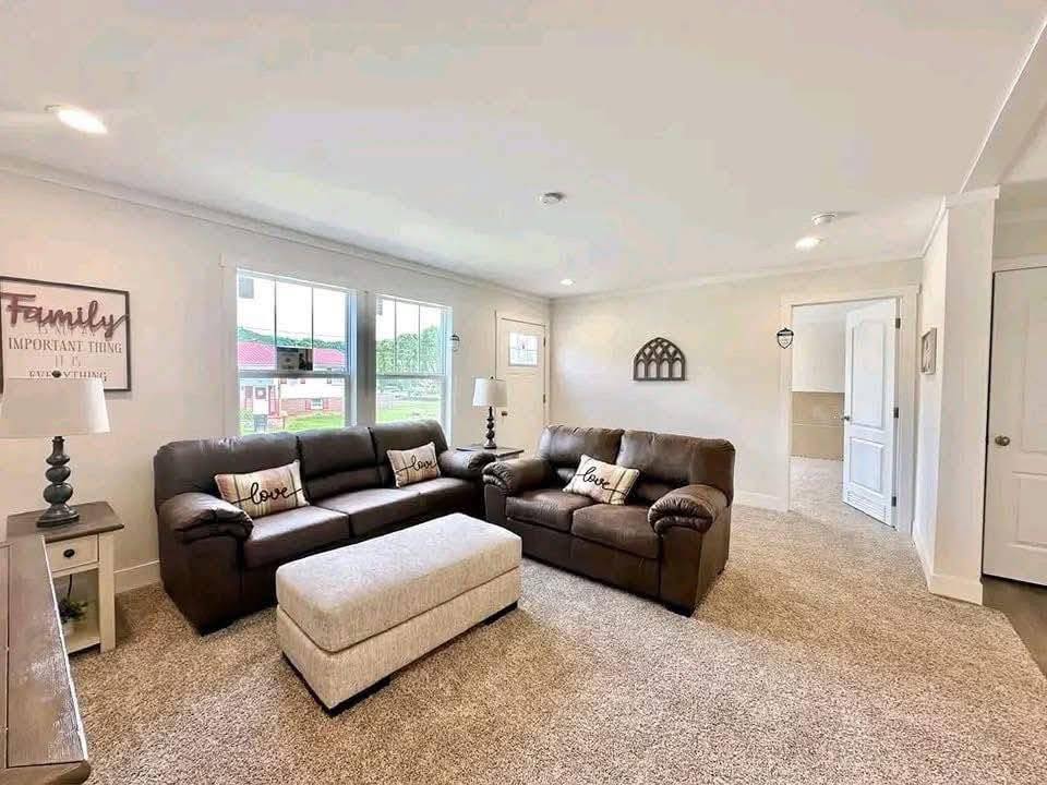Bright living room with brown leather sofas, a beige ottoman, and pillows with "love." A sign says "Family, most important thing." Soft, inviting atmosphere.