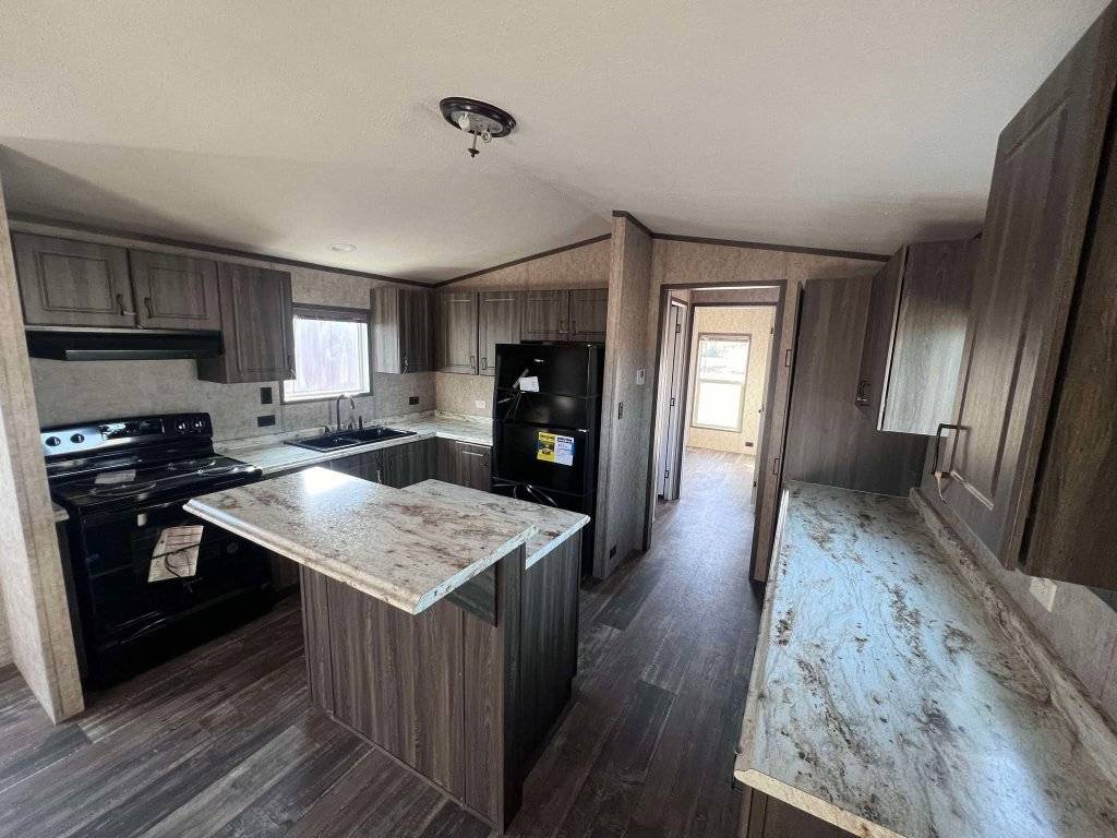 Modern kitchen with dark wood cabinets and marble countertops. Features a black stove, fridge, and island. Bright, clean, and spacious.