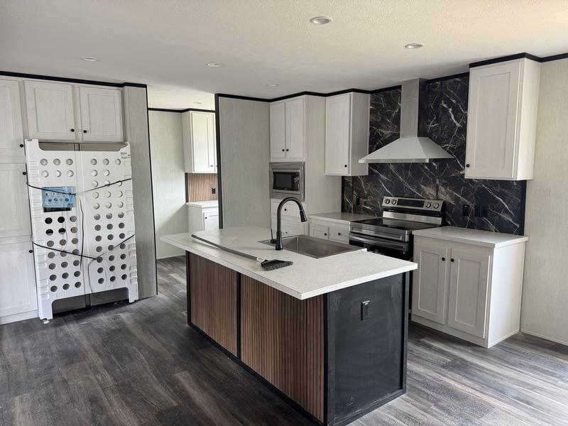 Modern kitchen with a central island featuring a white countertop and black sink. Stainless steel appliances contrast with black marble backsplash. Light wooden cabinets surround, offering a sleek and elegant atmosphere.