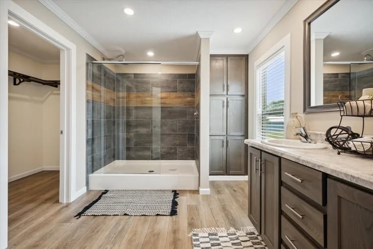 Modern bathroom with wood flooring, a glass-enclosed shower with slate tiles, a double-sink vanity, and a large mirror. Bright and spacious.