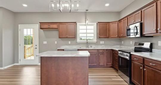 Modern kitchen with dark wood cabinets, marble countertops, and stainless steel appliances. Island in center, door to patio on left, soft lighting.