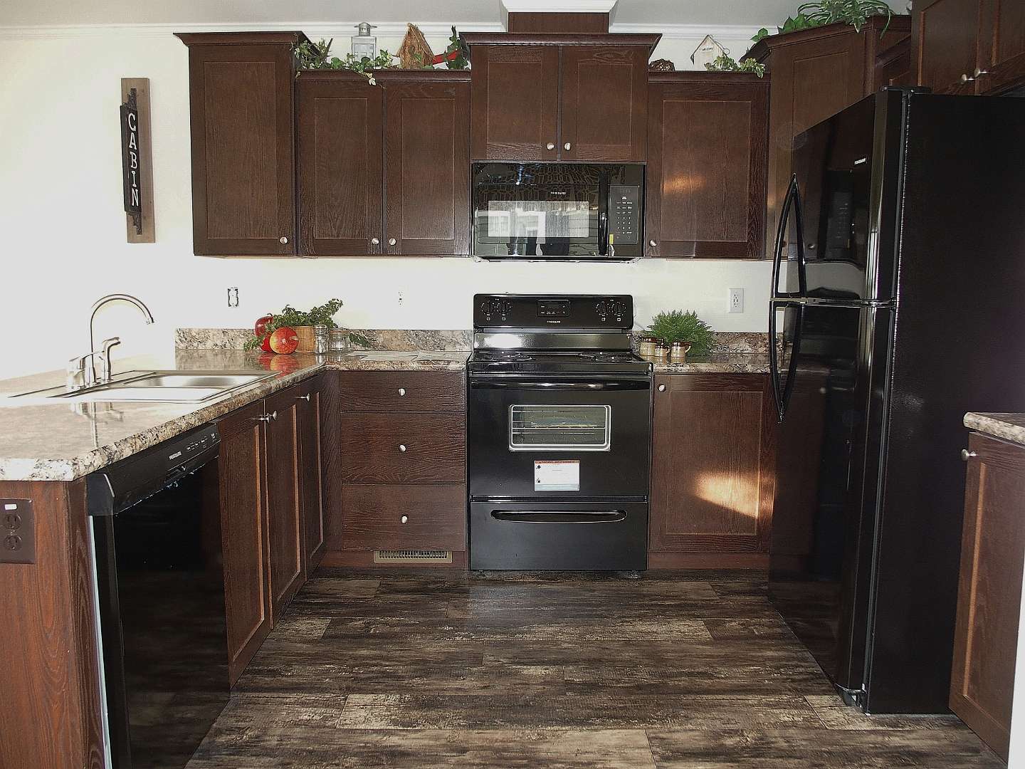 Warm kitchen with dark wood cabinets, granite countertops, and stainless steel appliances. A cozy, inviting atmosphere with plants and decor.