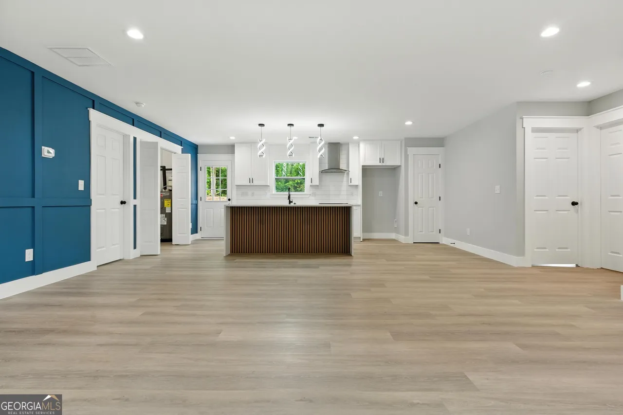 Spacious open-concept kitchen and living area with light wood flooring, blue accent wall, modern kitchen island, white cabinets, and pendant lights.
