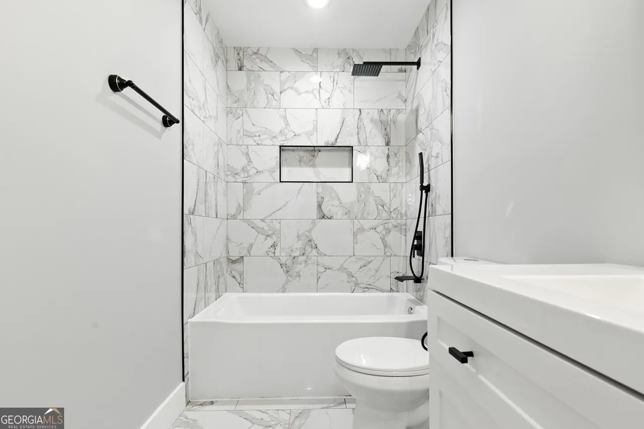 Sleek bathroom with white and grey marble tiles. Features a bathtub, modern black fixtures, a window niche, and a white vanity. Bright and minimalistic.