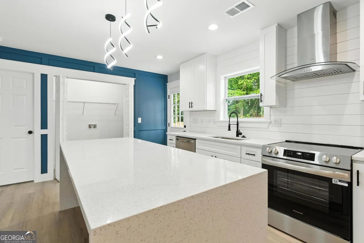 Modern kitchen with a large white island, sleek black fixtures, and stainless steel appliances. Blue accent wall adds contrast to white cabinetry.