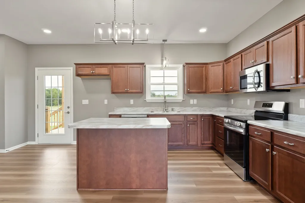 Modern kitchen with light wood flooring, brown cabinets, and white countertops. Features an island, stainless steel appliances, and large window.