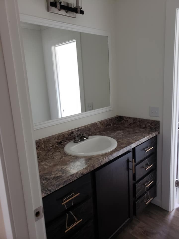Bathroom with a modern vanity featuring a dark cabinet, marble countertop, and white sink. A large mirror and wall light fixture create a clean, bright look.