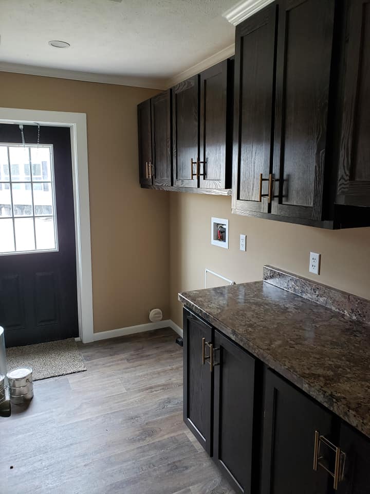 Modern kitchen with dark wooden cabinets, granite countertops, and beige walls. A glass door allows natural light, creating a cozy and inviting atmosphere.