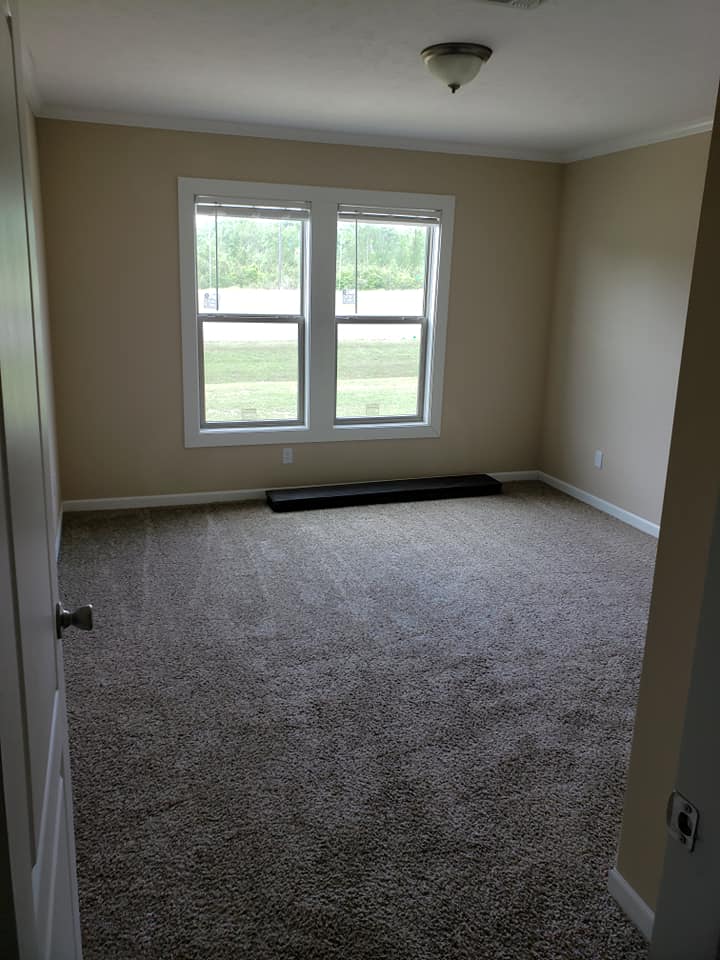 Empty beige room with light tan carpet, featuring two large windows. Natural light creates a calm atmosphere, softly illuminating the space.