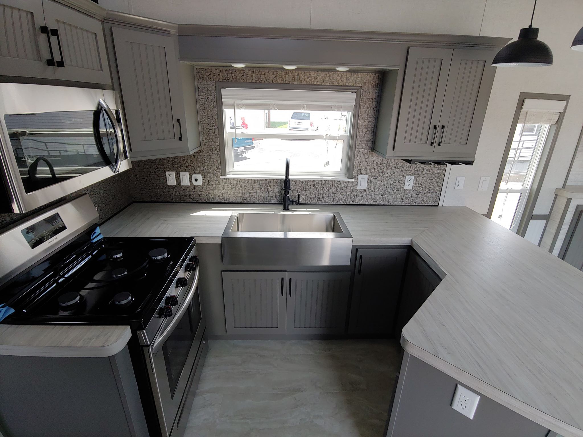 Modern kitchen with gray cabinetry, a stainless steel stove and sink, under-cabinet lighting, and a tiled backsplash. Bright, clean, and inviting.