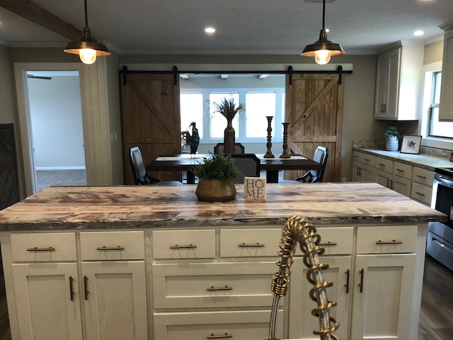 Cozy kitchen with a rustic vibe featuring a large island with wood countertop, pendant lights, and barn doors leading to a dining area, evoking warmth.