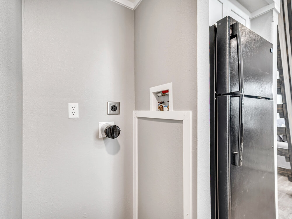 Nook in a kitchen featuring gray walls, washer/dryer hookups, and adjacent black refrigerator. Space awaits appliances, conveying a neat, organized vibe.