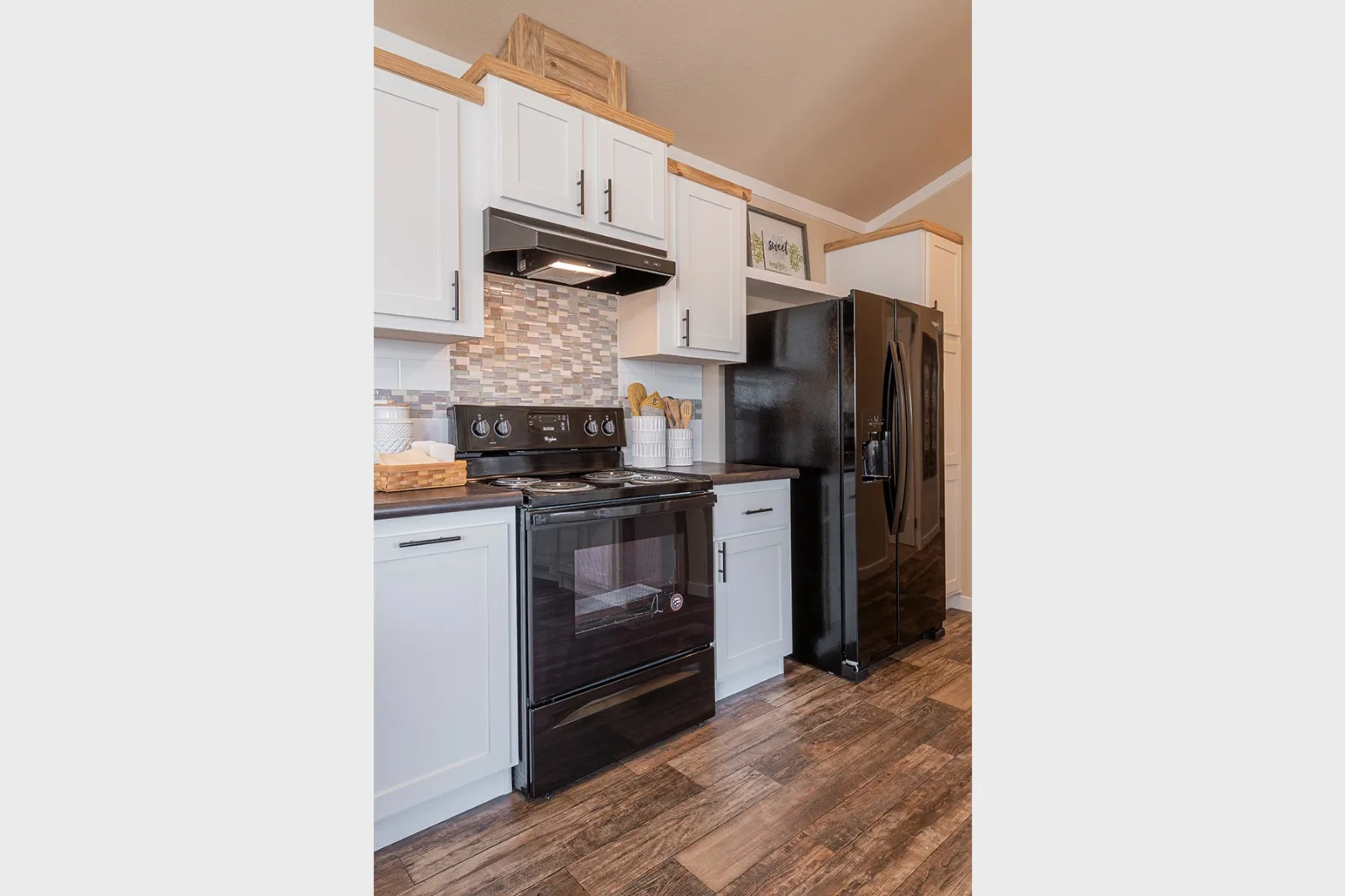 Modern kitchen features white cabinets, black appliances including a stove and fridge, wood flooring, and a tiled backsplash, creating a sleek look.