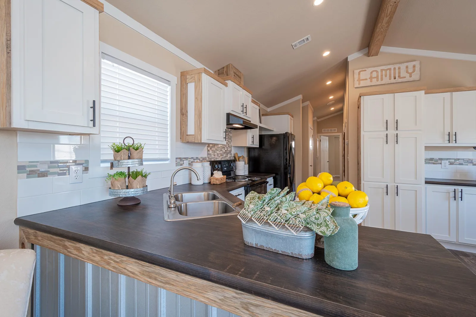 Modern kitchen with white cabinets, dark countertops, and stainless steel sink. A basket of lemons and a vase add vibrant accents. Cozy and inviting atmosphere.