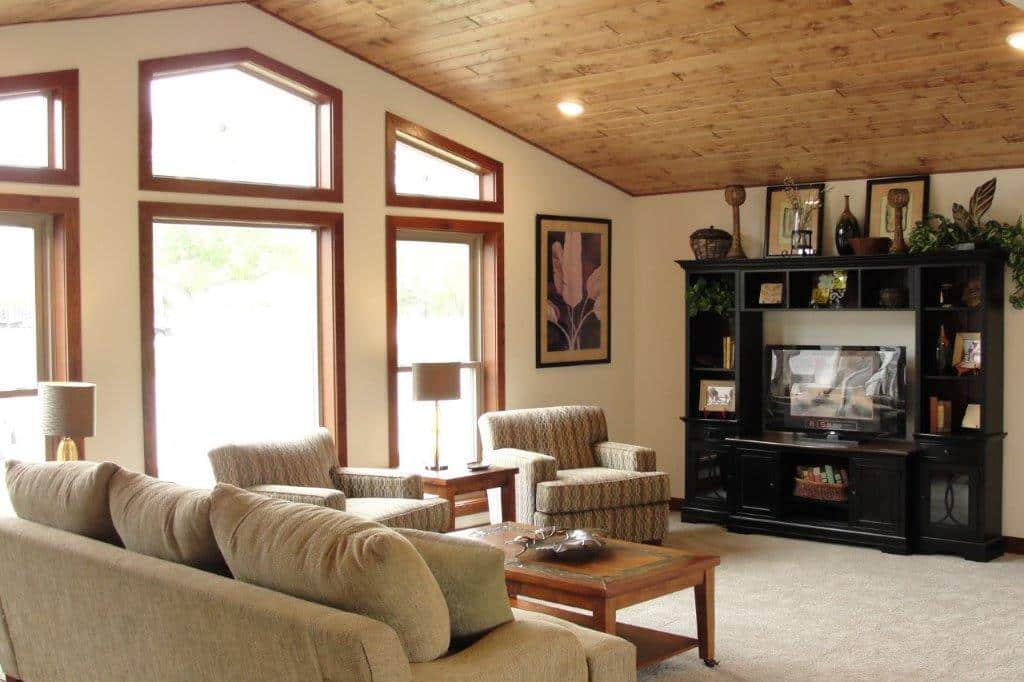 Spacious living room with beige sofas, armchairs, and wood accents. Large windows bring in natural light. Shelves with decor and a cozy, warm atmosphere.