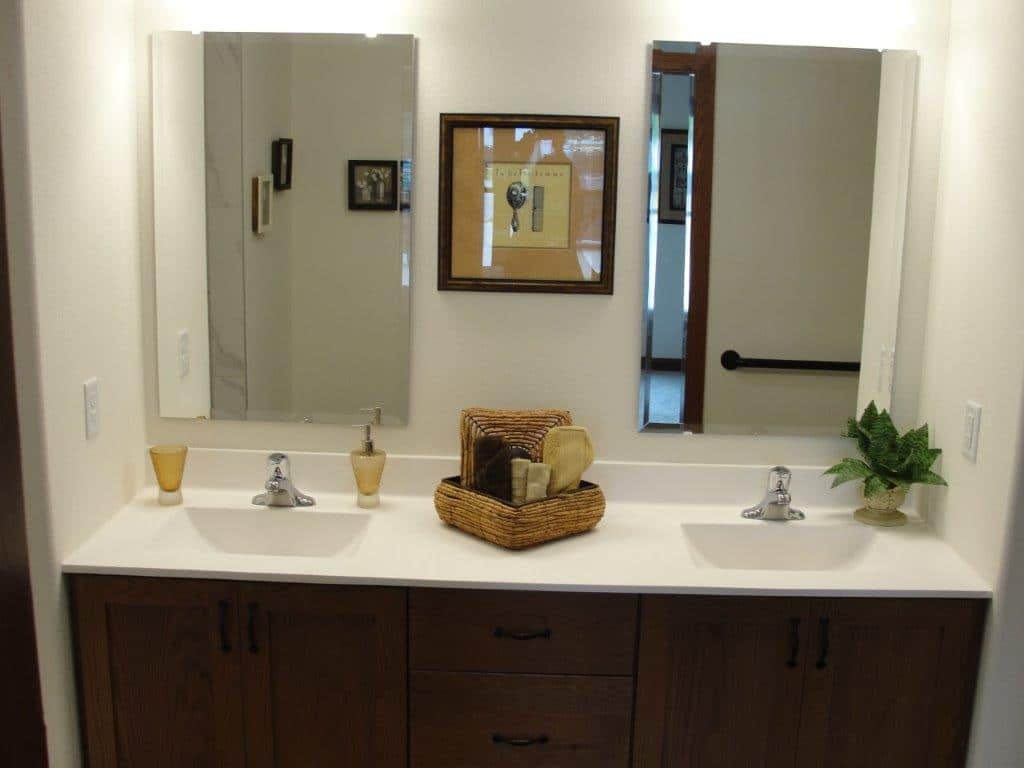 Double-sink bathroom vanity with wood cabinetry, two mirrors, potted plant, and wicker basket with toiletries; light and clean atmosphere.