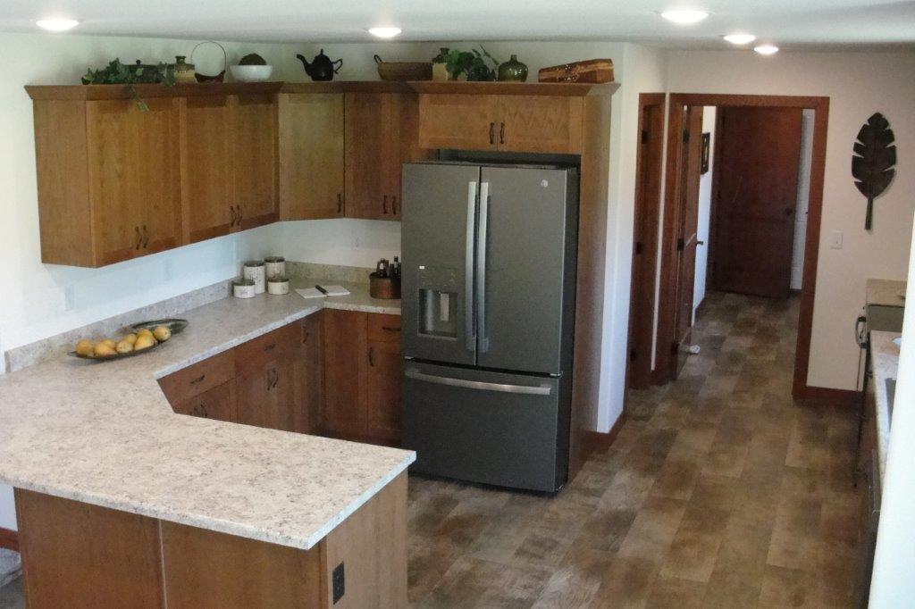 Modern kitchen with wooden cabinets, stainless steel fridge, and beige granite countertops. Decor includes potted plants. Warm, inviting tone.
