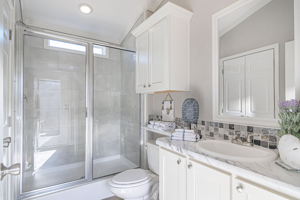 Bright bathroom with glass shower, white vanity with marble top, and decorative tiles. Neat towels, lavender, and a serene ambiance.