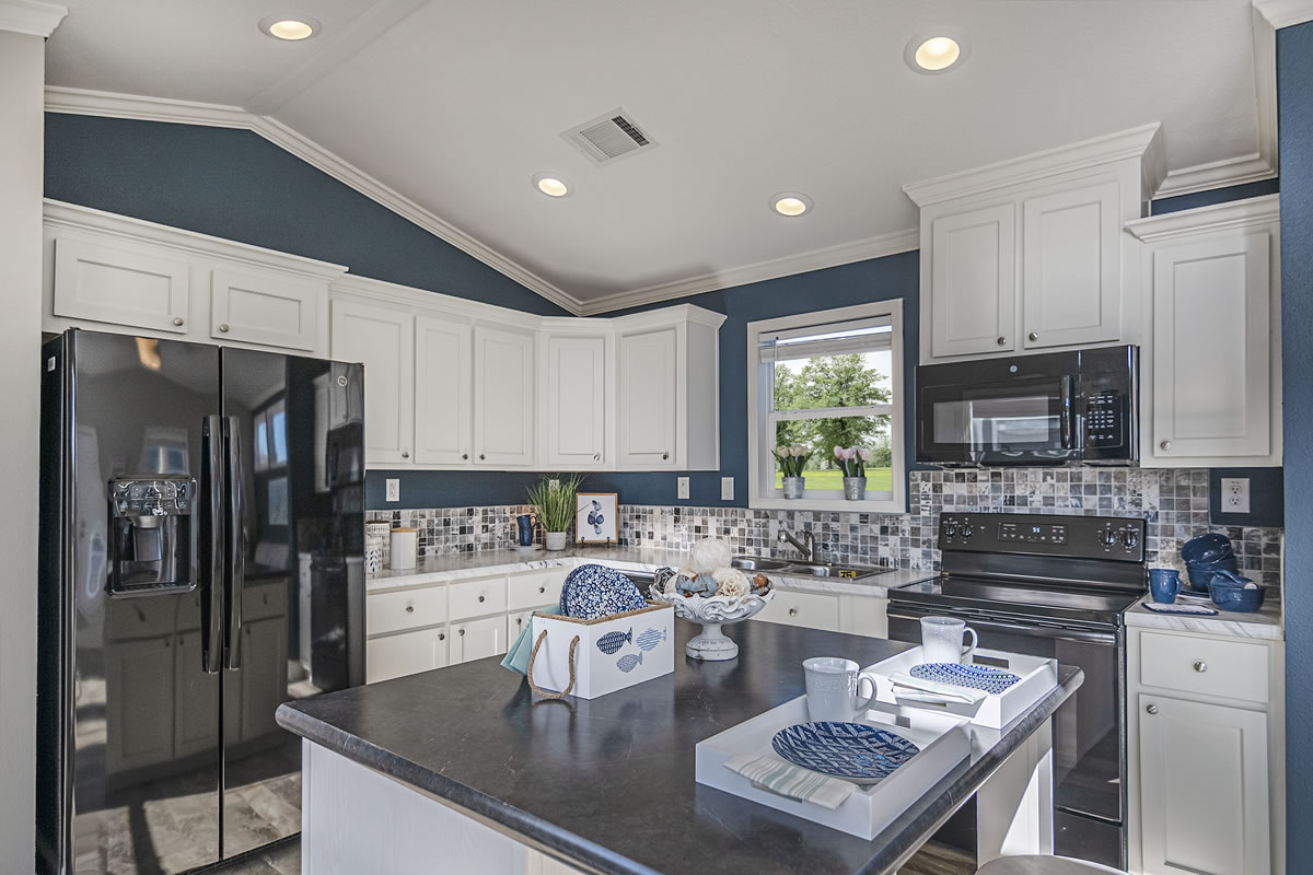 Modern kitchen with white cabinets, dark countertops, and blue accents. Black appliances and a small island decorated with plates and cups create a clean, inviting atmosphere.